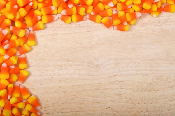 Corner boarder of candy corn on a light wood background with copy space. Candy corn is a candy most often found in the United States and Canada, popular primarily around Halloween