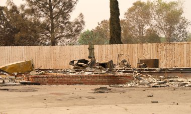 Ev yanıp kül olmuş, çitlere dokunulmamış. Redding, California 'daki son yangın fırtınasında. Ateş kilometrelerce uzakta yanmaya devam ederken duman ve kül havada..