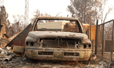 Redding, Ca 'da yakın zamanda çıkan yangında evin önündeki tel örgülerin yanında yanmış bir araba yanmış. Ateş kilometrelerce uzakta yanmaya devam ederken duman ve kül havada..