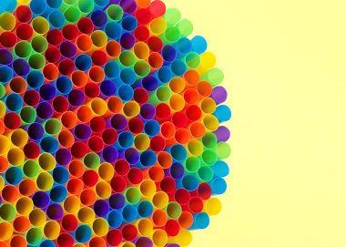 Yüzlerce renkli plastik kamışın yüzleri öne dönük şekilde uzanmış, sarı yüzeye uzanmış, izleyiciye doğru açılmış şekilde. Birçok şehir artık tek kullanımlık plastik pipetleri yasaklıyor..