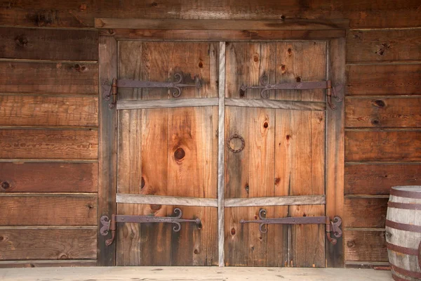 Paslı donanımlı eski ahşap çift kapılı kapılar, kapının yanına istiflenmiş ahşap variller. Kapat..