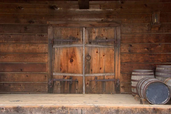 Paslı donanımlı eski ahşap çift kapılı kapılar, kapının yanına istiflenmiş ahşap variller..