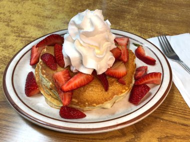 Yansıtıcı ahşap masaya krep, çilek ve kremayla kaplı bir tabak. Popüler Amerikan kahvaltısı.