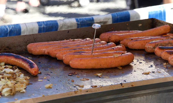 Large hot dogs on an outdoor grill cooking, food thermometer in one weiner to verify temperature meets minimum for healthy cooked food. Street vendor, close up on stove.