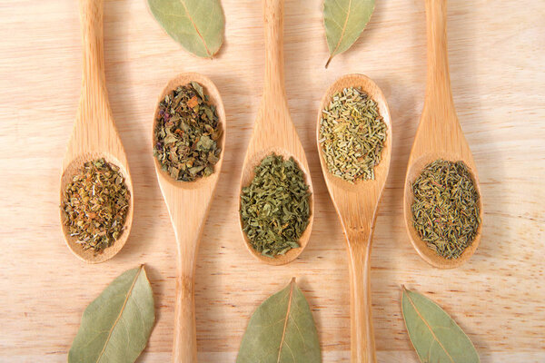 Wooden spoons with traditional Italian herbs for cooking on a light wood table.