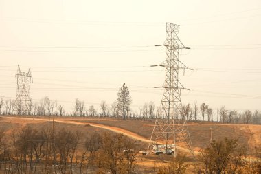 Redding, Ca - 06 Ağustos 2018: PG ve E ekipleri Carr yangınının ardından büyük ölçüde yok olan bölgedeki elektrik hatları üzerinde çalışıyorlar. Ateş kilometrelerce uzakta yanmaya devam ederken duman ve kül havada..