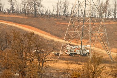 Redding, Ca - 06 Ağustos 2018: PG ve E ekipleri Carr yangınının ardından büyük ölçüde yok olan bölgedeki elektrik hatları üzerinde çalışıyorlar. Ateş kilometrelerce uzakta yanmaya devam ederken duman ve kül havada..