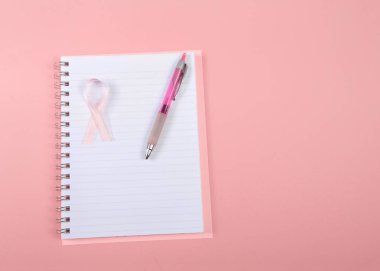 Beyaz çizgili dizüstü bilgisayarda pembe arka planda göğüs kanseri farkındalığı için fotokopi alanı olan pembe kalemle Pembe kurdelenin üzerinde düz bir görünüm 