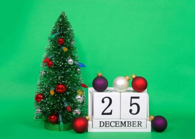 Tahta bloklar 25 Aralık Noel 'i, yanında küçük süslenmiş Xmas ağacı olan yeşil bir arka planda otururken, üzerinde ve yanında birkaç sokak süsleri olan takvim tarihini gösteriyor..