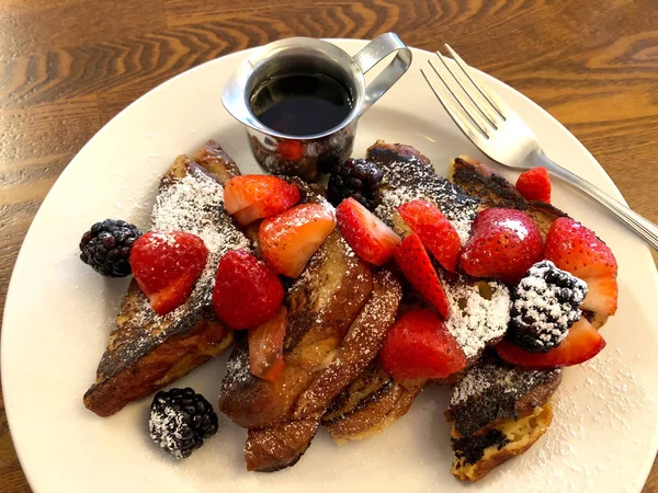 Kahvaltı, yanında çilek ve böğürtlen ile Fransız tostu beyaz tabakta, ahşap masa, yanına da çatal bıçak..