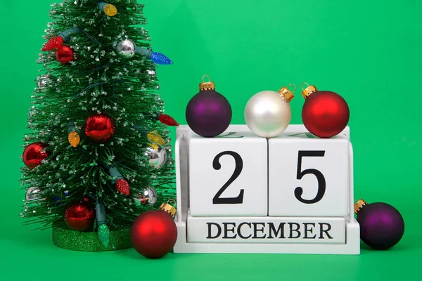 Ahşap blokların kapatılması 25 Aralık, Noel, yeşil arka planda oturan, yanında küçük süslenmiş Xmas ağacı, üzerinde ve yanında birkaç sokak süsleri olan takvim tarihini gösterir.