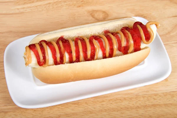 Banana with peanut butter and jelly in a hot dog bun served on a white rectangular plate served on a wood table. Top view from an angle