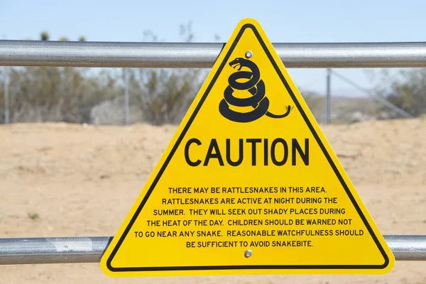 A yellow triangle sign with Snake caution warning at a rest top in the desert along a California Highway