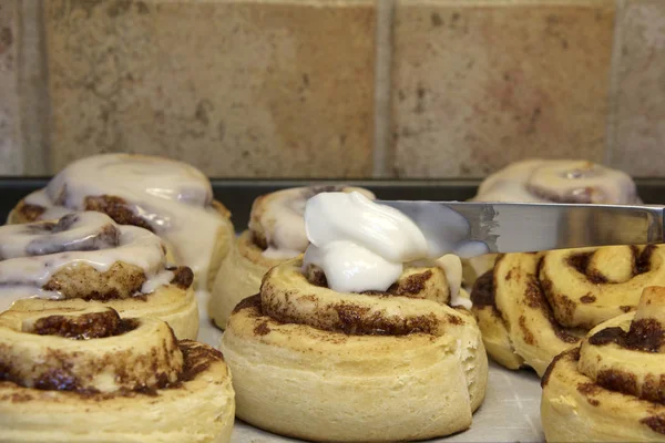 Hot homemade cinnamon rolls fresh out of the oven, knife applyin — Stock Photo, Image