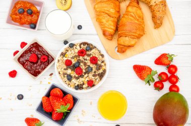 Tereyağlı kruvasanla kahvaltı, tahıllı mısır gevreği ve çilek, yabanmersini, ahududu, kivi, C vitamini ve ahşap masada sağlıklı yiyecekler.