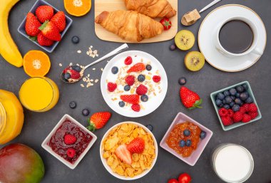 Tereyağlı kruvasanla kahvaltı, tahıllı mısır gevreği ve çilek, yabanmersini, ahududu, kivi, C vitamini ve ahşap masada sağlıklı yiyecekler.