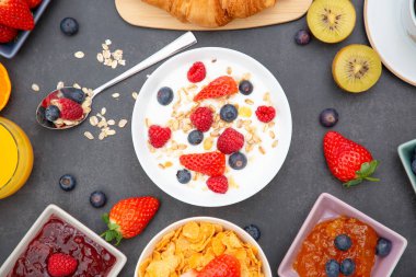 Tereyağlı kruvasanla kahvaltı, tahıllı mısır gevreği ve çilek, yabanmersini, ahududu, kivi, C vitamini ve ahşap masada sağlıklı yiyecekler.