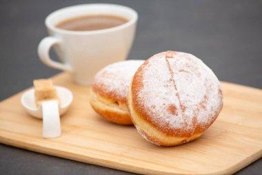 Tatlı, donut, çikolata ve çilek halkaları, şekerli ve kremalı çörekler ve sıcak kahve fincanları, ahşap masa arkasında kırılma veya parti hazırlığı.