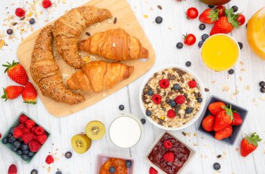 Kahvaltıda yanında tereyağlı kruvasan, mısır gevreği, fincanda süt, çilek, ahududu, kivi, kahvaltı masasında taze portakal suyu....