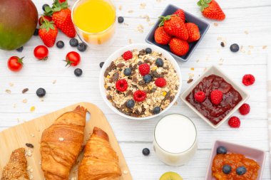 Kahvaltıda yanında tereyağlı kruvasan, mısır gevreği, fincanda süt, çilek, ahududu, kivi, kahvaltı masasında taze portakal suyu....