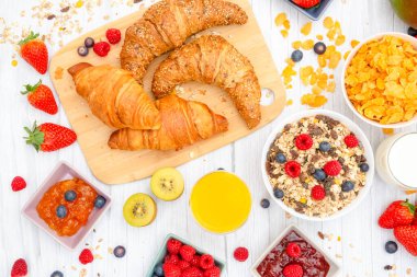 Kahvaltıda yanında tereyağlı kruvasan, mısır gevreği, fincanda süt, çilek, ahududu, kivi, kahvaltı masasında taze portakal suyu....