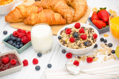 Kahvaltıda yanında tereyağlı kruvasan, mısır gevreği, fincanda süt, çilek, ahududu, kivi, kahvaltı masasında taze portakal suyu....