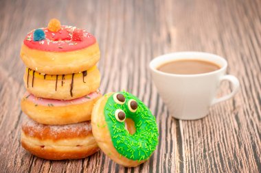 Tatlı, donut, çikolata ve çilek halkaları, şekerli ve kremalı çörekler ve sıcak kahve fincanları, ahşap masa arkasında kırılma veya parti hazırlığı.