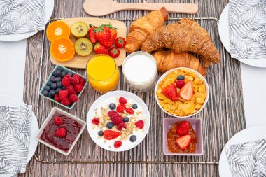 Kahvaltıda meyveli yoğurt, tereyağlı kruvasan, mısır gevreği, fincanda süt, çilek, ahududu, kivi ve kahvaltı masasında taze portakal suyu ile servis edilir.