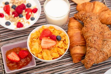 Kahvaltıda meyveli yoğurt, tereyağlı kruvasan, mısır gevreği, fincanda süt, çilek, ahududu, kivi ve kahvaltı masasında taze portakal suyu ile servis edilir.