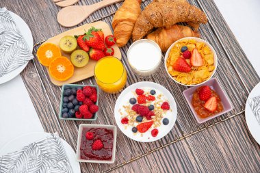Kahvaltıda meyveli yoğurt, tereyağlı kruvasan, mısır gevreği, fincanda süt, çilek, ahududu, kivi ve kahvaltı masasında taze portakal suyu ile servis edilir.