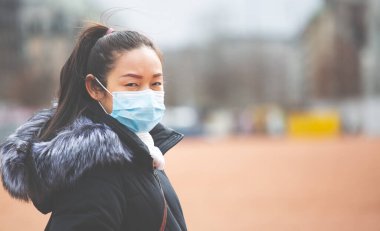 Mikropları, zehirli dumanları ve tozu önlemek için maske takan genç bir Asyalı kadının görüntüsü. Sokaklarda ve bahçelerde bakteriyel enfeksiyonun önlenmesi.