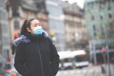 Mikropları, zehirli dumanları ve tozu önlemek için maske takan genç bir Asyalı kadının görüntüsü. Sokaklarda ve bahçelerde bakteriyel enfeksiyonun önlenmesi.