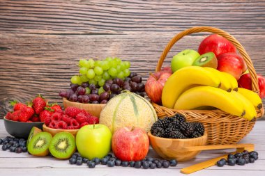 Muz, kivi, üzüm, ahududu, böğürtlen ve böğürtlenli C vitamini ile ahşap sepetteki sağlıklı meyve grubu..