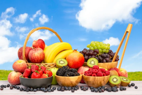 Group Healthy fresh fruit in a wooden basket, With vitamins c from bananas, kiwi, grapes, raspberries, blueberries, and blackberries, good for the body and diet food on the table in nature background.