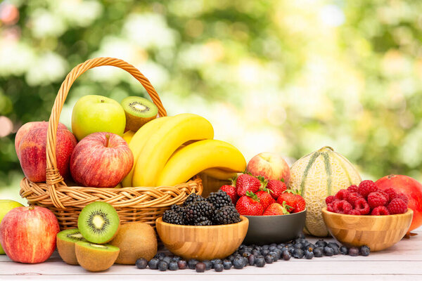 Group Healthy fresh fruit in a wooden basket, With vitamins c from bananas, kiwi, grapes, raspberries, blueberries, and blackberries, good for the body and diet food on the table in nature background.