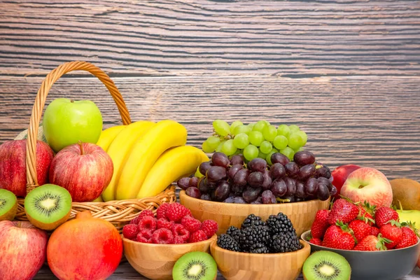 Muz, kivi, üzüm, ahududu, böğürtlen ve böğürtlenli C vitamini ile ahşap sepetteki sağlıklı meyve grubu..