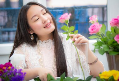 Kırmızı ve pembe gülleri budamaya hazırlanan bir kadın ve evdeki güzel çiçek aranjmanları, masadaki aile içinde Sevgililer Günü ve İş için vazo ile çiçek aranjmanları.