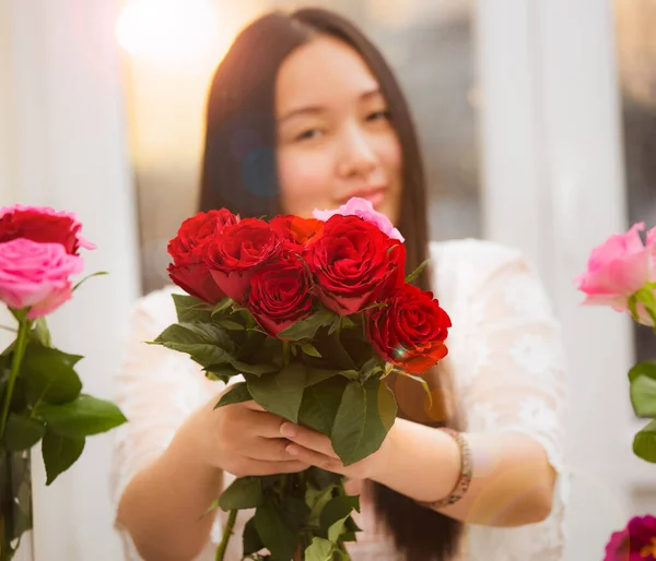 Kırmızı ve pembe gülleri budamaya hazırlanan kadın ve evdeki güzel çiçek aranjmanları Sevgililer Günü için vazoyla çiçek aranjmanları ve masada aile içi hediyeler.