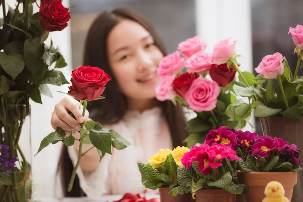 Kırmızı ve pembe gülleri budamaya hazırlanan kadın ve evdeki güzel çiçek aranjmanları Sevgililer Günü için vazoyla çiçek aranjmanları ve masada aile içi hediyeler.