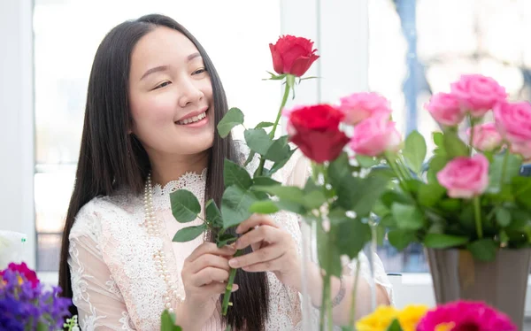 Kırmızı ve pembe gülleri budamaya hazırlanan bir kadın ve evdeki güzel çiçek aranjmanları, masadaki aile içinde Sevgililer Günü ve İş için vazo ile çiçek aranjmanları.