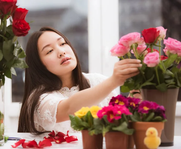 Kırmızı ve pembe gülleri budamaya hazırlanan kadın ve evdeki güzel çiçek aranjmanları Sevgililer Günü için vazoyla çiçek aranjmanları ve masada aile içi hediyeler.