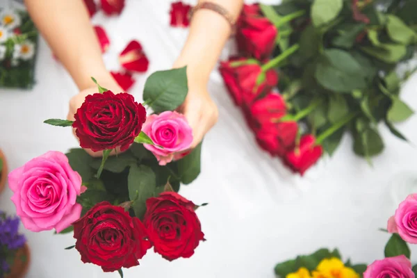 Kırmızı ve pembe gülleri budamaya hazırlanan bir kadın ve evdeki güzel çiçek aranjmanları, masadaki aile içinde Sevgililer Günü ve İş için vazo ile çiçek aranjmanları.