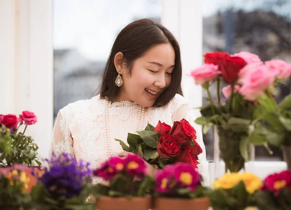 Kırmızı ve pembe gülleri budamaya hazırlanan bir kadın ve evdeki güzel çiçek aranjmanları, masadaki aile içinde Sevgililer Günü ve İş için vazo ile çiçek aranjmanları.