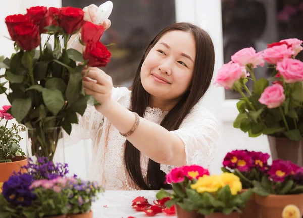 Kırmızı ve pembe gülleri budamaya hazırlanan kadın ve evdeki güzel çiçek aranjmanları Sevgililer Günü için vazoyla çiçek aranjmanları ve masada aile içi hediyeler.