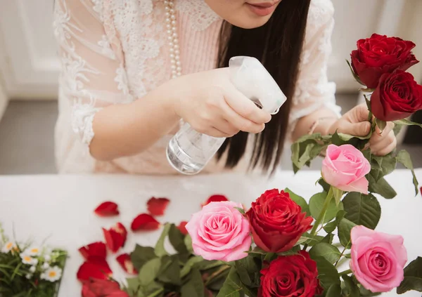 Kırmızı ve pembe gülleri budamaya hazırlanan bir kadın ve evdeki güzel çiçek aranjmanları, masadaki aile içinde Sevgililer Günü ve İş için vazo ile çiçek aranjmanları.
