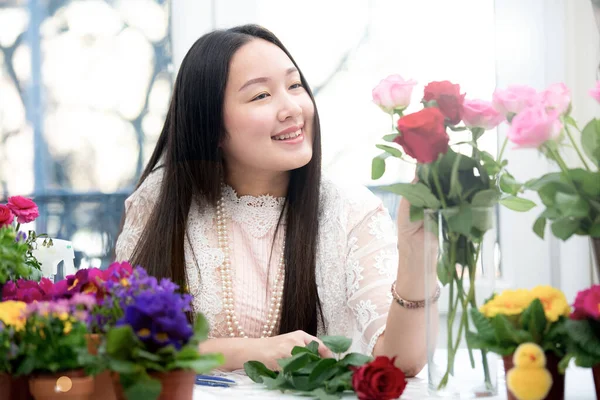 Kırmızı ve pembe gülleri budamaya hazırlanan bir kadın ve evdeki güzel çiçek aranjmanları, masadaki aile içinde Sevgililer Günü ve İş için vazo ile çiçek aranjmanları.