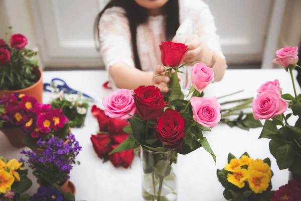 Kırmızı ve pembe gülleri budamaya hazırlanan bir kadın ve evdeki güzel çiçek aranjmanları, masadaki aile içinde Sevgililer Günü ve İş için vazo ile çiçek aranjmanları.