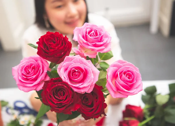 Kırmızı ve pembe gülleri budamaya hazırlanan bir kadın ve evdeki güzel çiçek aranjmanları, masadaki aile içinde Sevgililer Günü ve İş için vazo ile çiçek aranjmanları.
