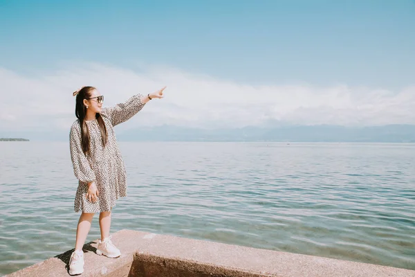 Beyaz tenli, uzun siyah saçlı, siyah gözlüklü güzel bir Asyalı kadın. Gökyüzü açık, turizm ve yaz tatillerinde taşın üzerine oturup göl manzarasını izlemekten mutluluk duyuyorum..
