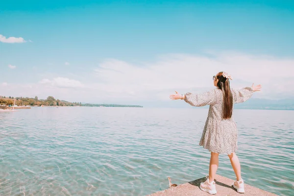 Beyaz tenli, uzun siyah saçlı, siyah gözlüklü güzel bir Asyalı kadın. Gökyüzü açık, turizm ve yaz tatillerinde taşın üzerine oturup göl manzarasını izlemekten mutluluk duyuyorum..